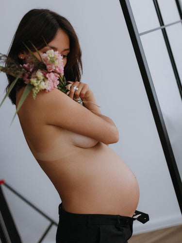 Smuk kvinde med stor gravid mave og en buket blomster i favnen 